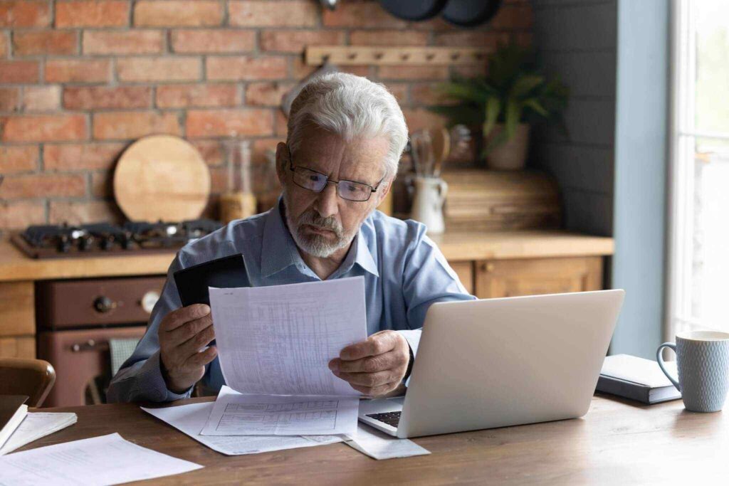Serious mature man wearing glasses calculating domestic bills at home