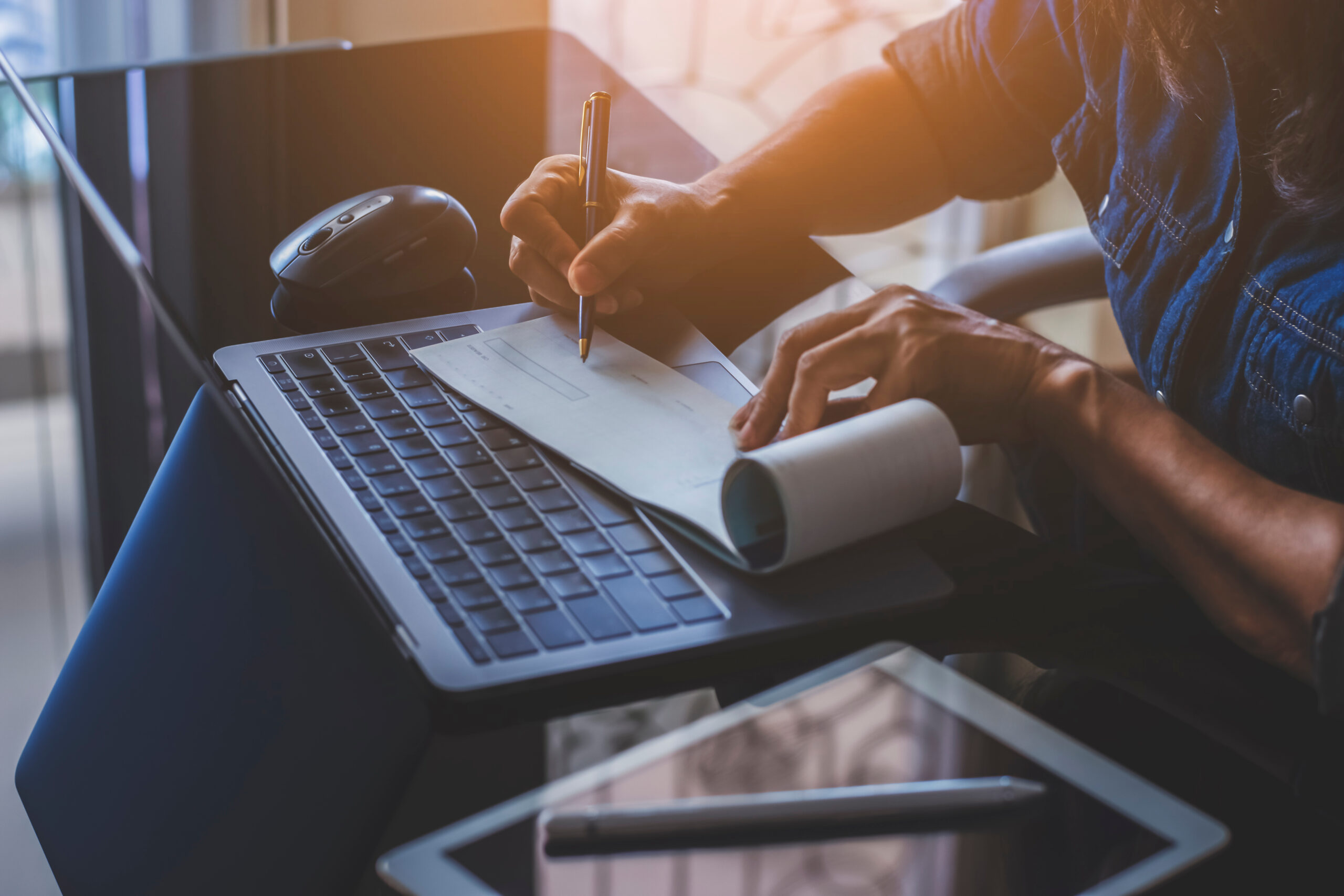 business woman handwriting a check with a laptop on a desk