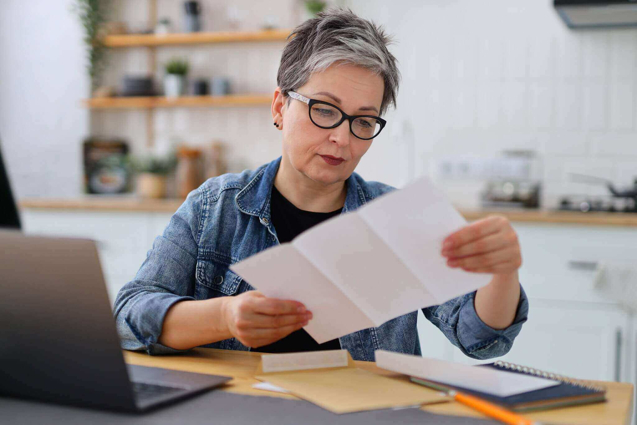 serious mature woman in glasses reading the bill in the kitchen