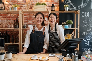 two asian women smiling behind the cashier counter of a small bakery