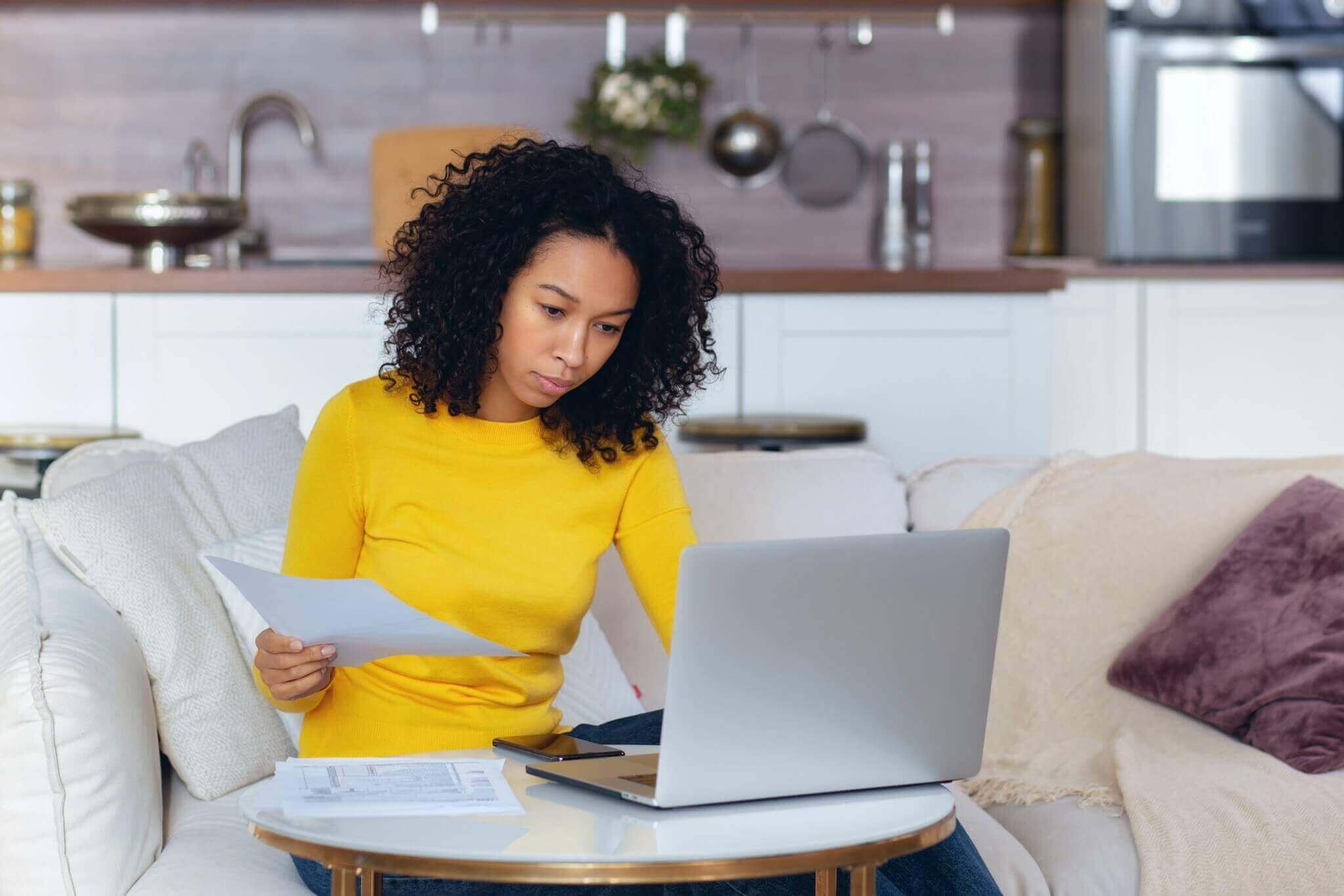 woman sitting at home on the couch looking through bills