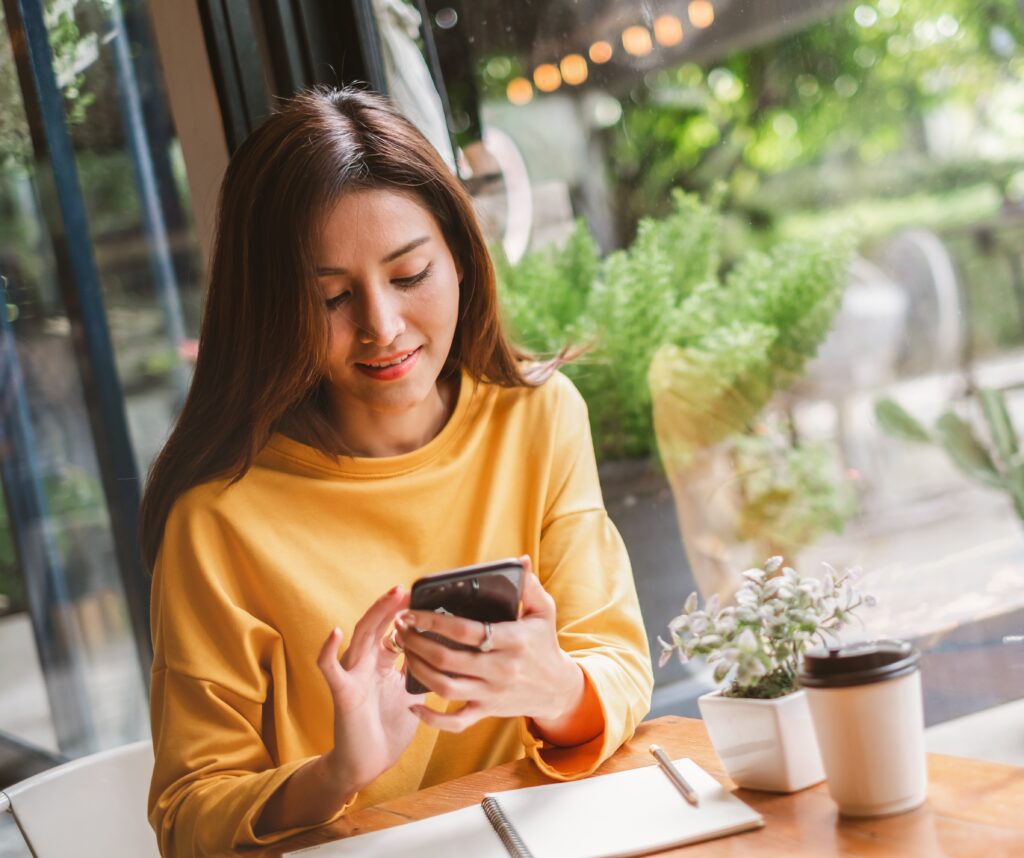 young women in a yellow sweater using phone for online banking