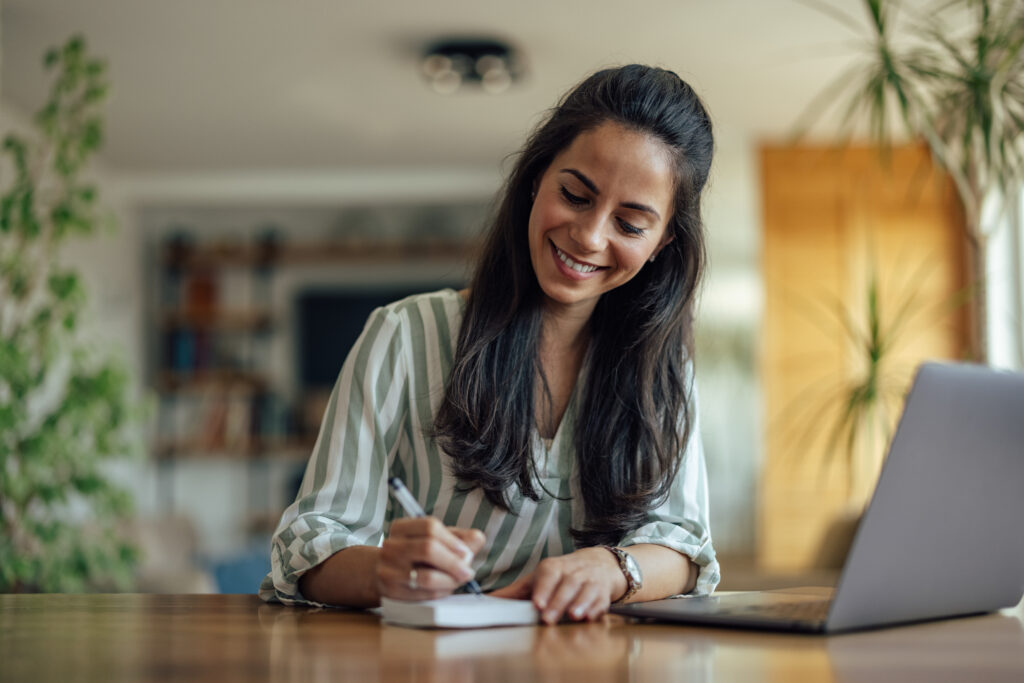 young women writing on a paper and using a laptop