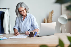 white business women in blue buttom up shirt writing on top of a desk