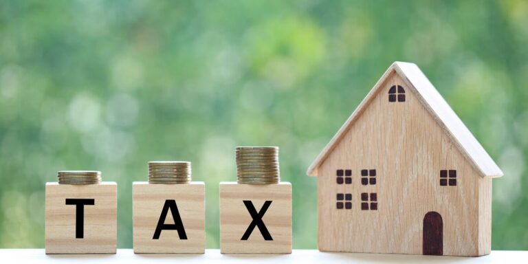 model house with stack of coins money and tax word on green background